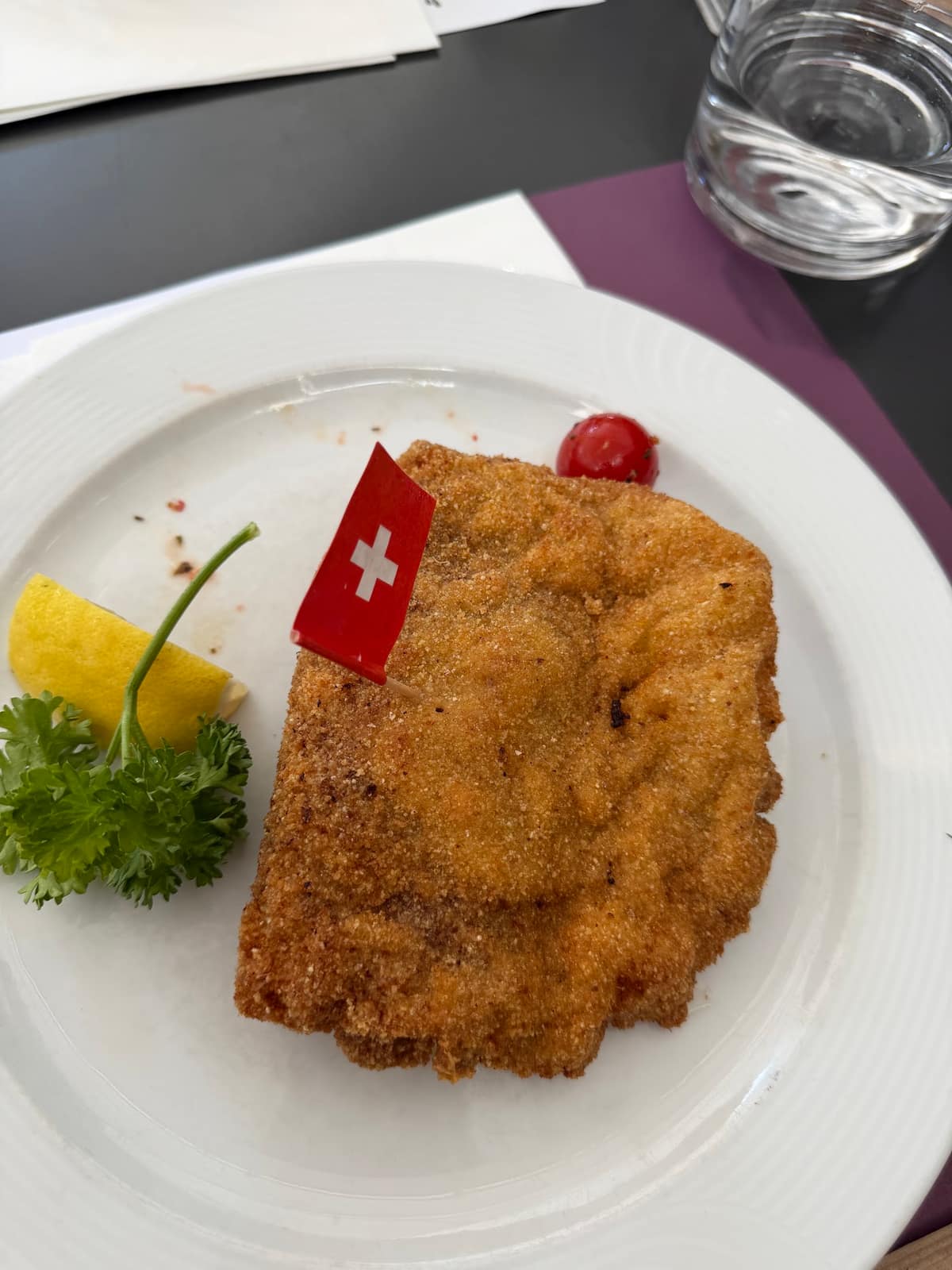 Une viande panée au Gifthüttli, avec un petit drapeau suisse, du citron et une tomate
