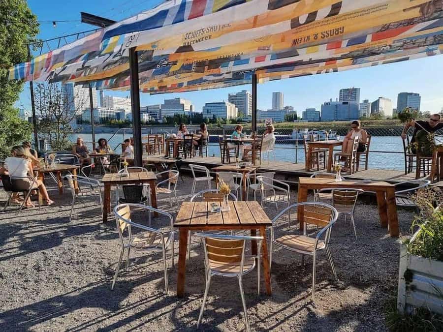 Die Terrasse der Landestelle unter bunten Sonnensegeln, dahinter der Rhein