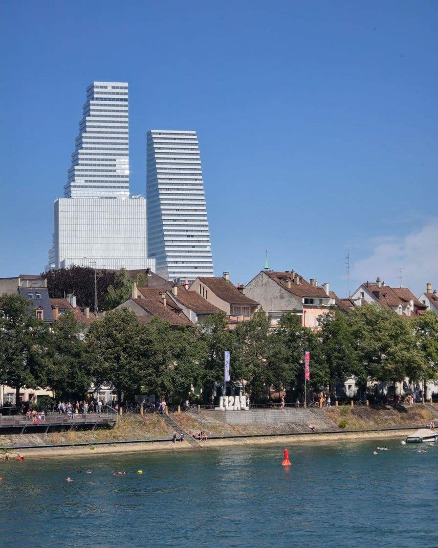 Der Rhein in Basel an einem Sommertag, hinter den Häusern am Ufer der Roche-Turm vor blauem Himmel