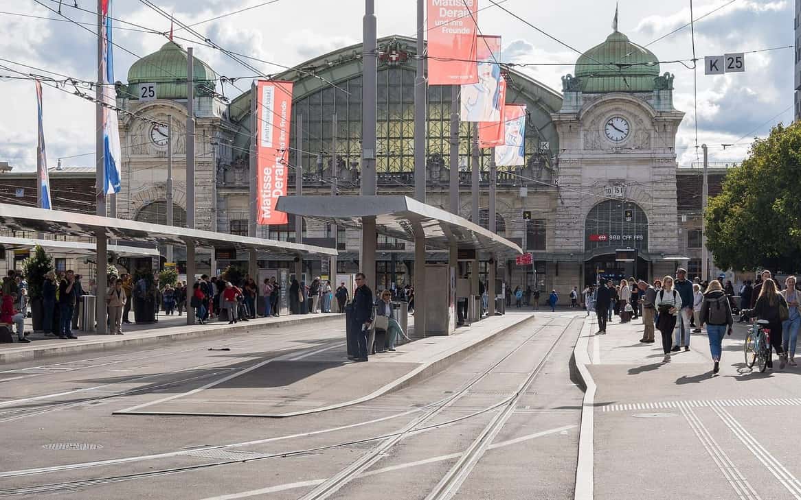 Das Empfangsgebäude des Bahnhofs Basel SBB am Centralbahnplatz mit seiner Uhr und der Tramstation davor