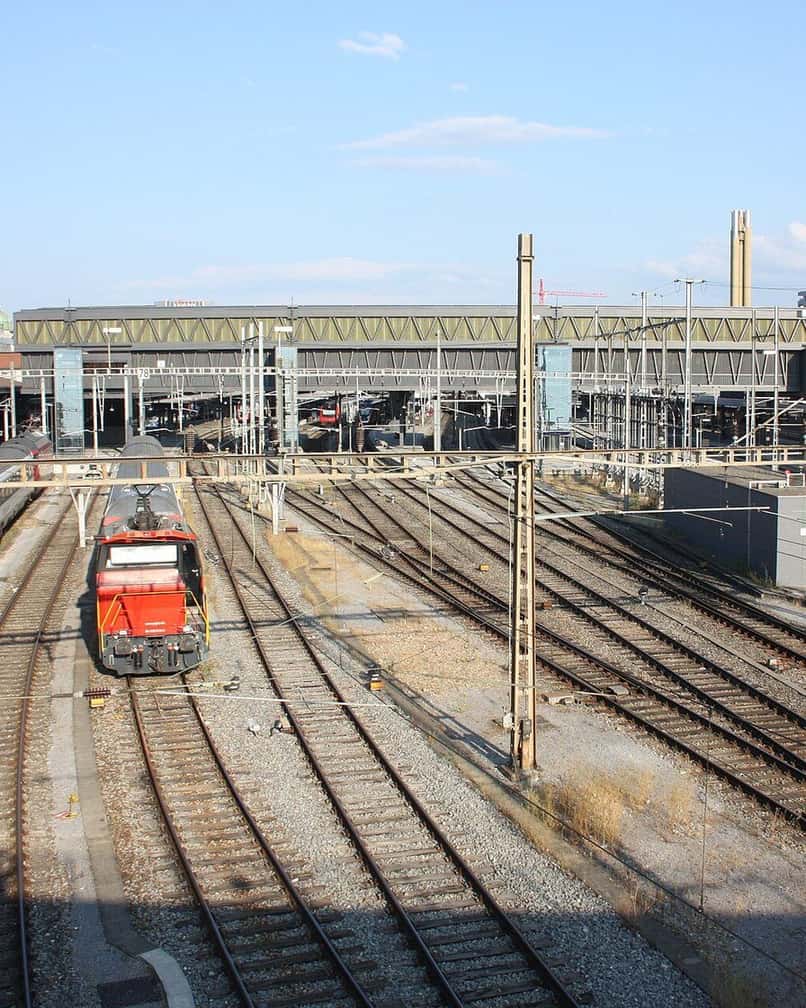 Das Gleisfeld des Bahnhofs Basel SBB mit einer roten Lokomotive unter den Fahrleitungen