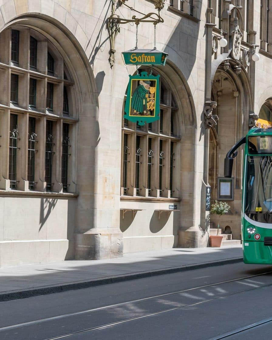 Ein grünes Basler Tram vor einem Gebäude aus Sandstein mit gotischen Fenstern