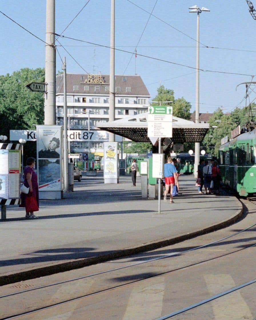 Eine Tramhaltestelle in Basel mit wartenden Fahrgästen und einem grünen Tram