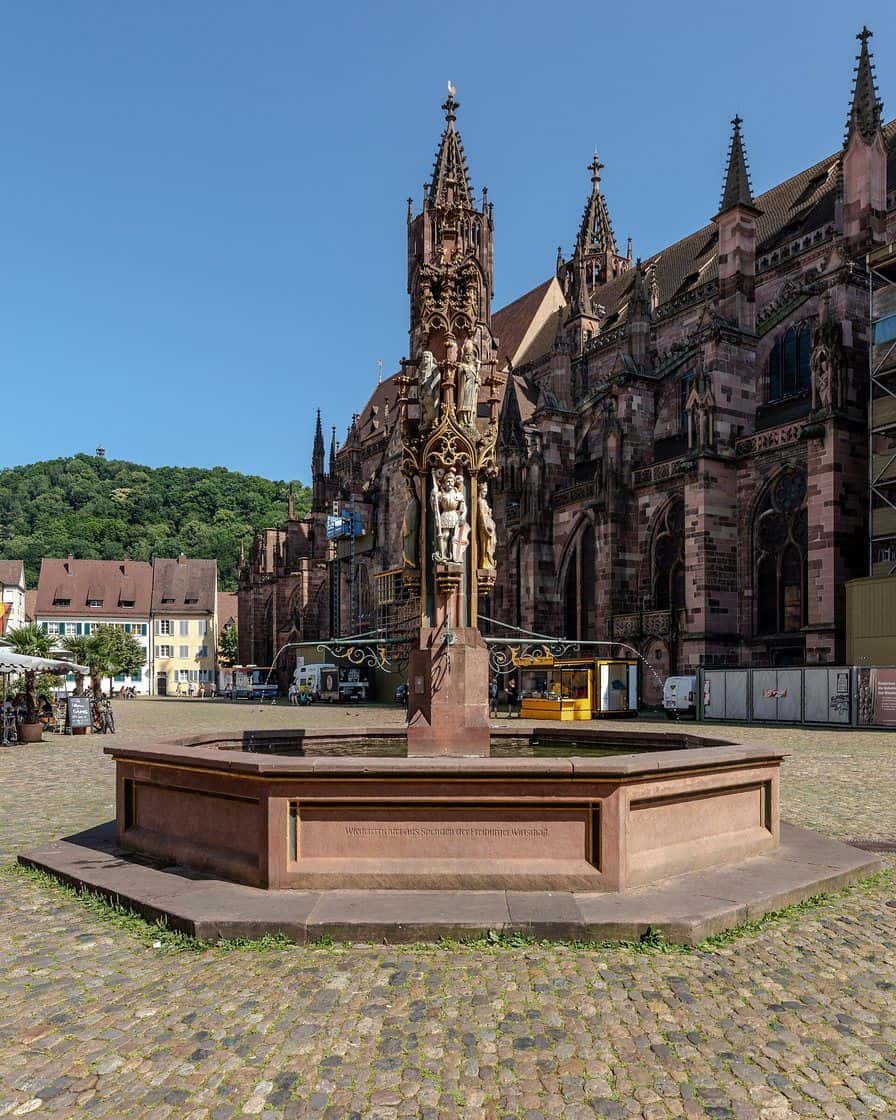 Der Münsterplatz in Freiburg im Breisgau mit dem Fischbrunnen und dem gotischen Münster aus rotem Sandstein