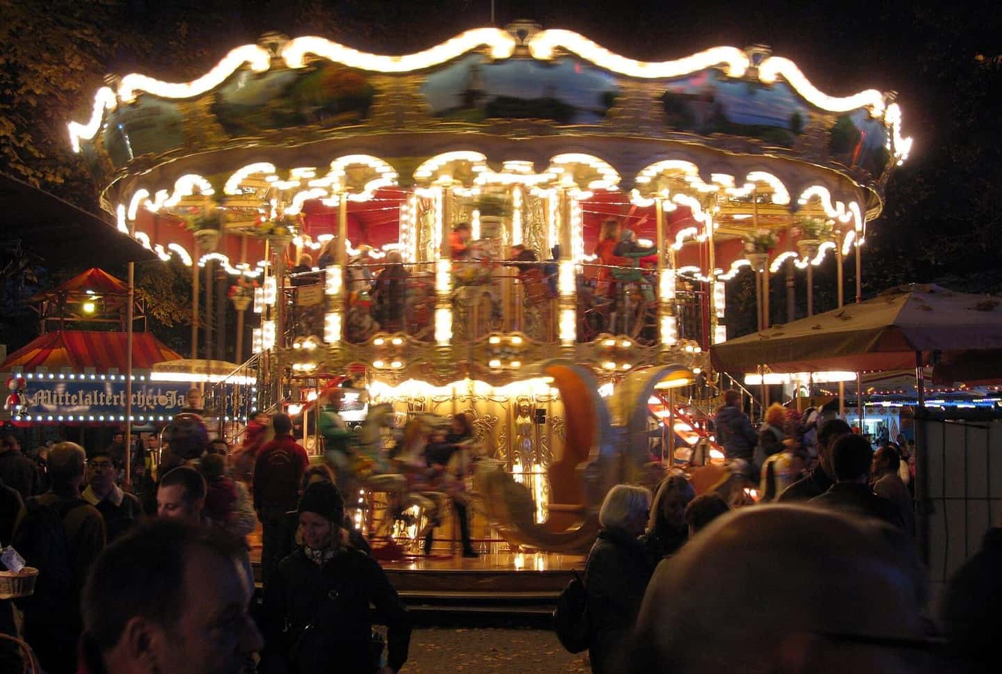 Ein beleuchtetes Karussell der Herbstmesse auf dem Petersplatz in Basel am Abend, davor Besucher