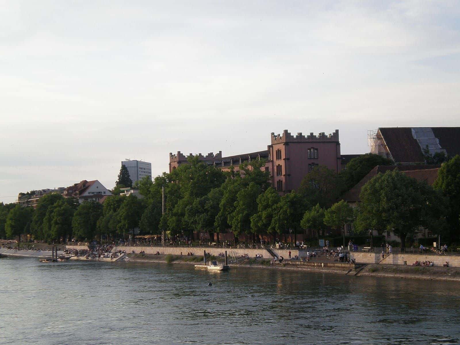Die Kaserne Basel in Kleinbasel vom Rhein aus gesehen, das Kasernengebäude mit Türmchen hinter den Bäumen der Uferpromenade