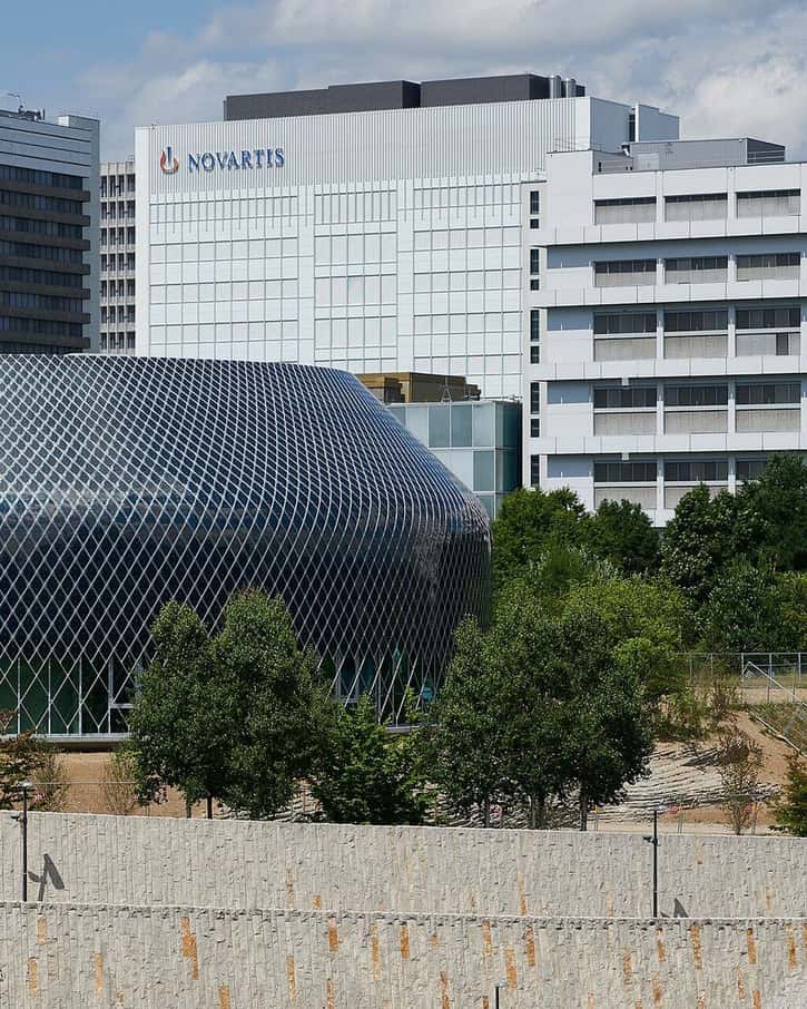 Le Novartis Pavillon, rond, à Bâle, avec son enveloppe sombre de modules solaires entre les bâtiments du campus