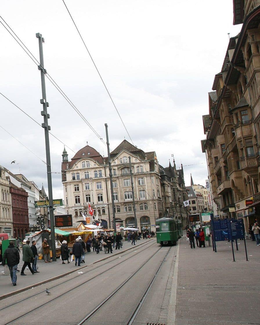 Der Marktplatz in Basel mit Marktständen, einem grünen Tram und den Geschäftshäusern an der Nordseite