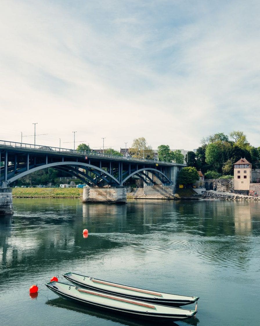 Eine Brücke über den Rhein in Basel, darunter zwei Boote am Ufer und ruhiges Wasser an einem hellen Morgen