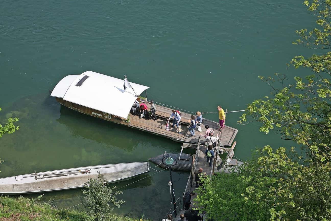 Die Münsterfähre «Leu» am Steg, Fahrgäste steigen ein, daneben ein Ruderboot