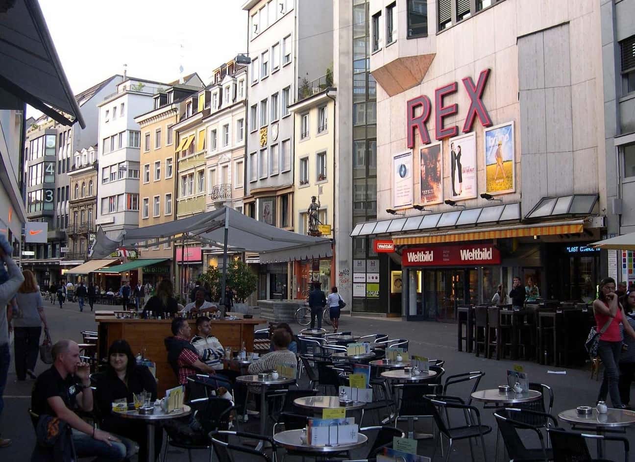 Die Steinenvorstadt in Basel mit Restaurantterrassen, Gästen an Tischen und dem Kino Rex