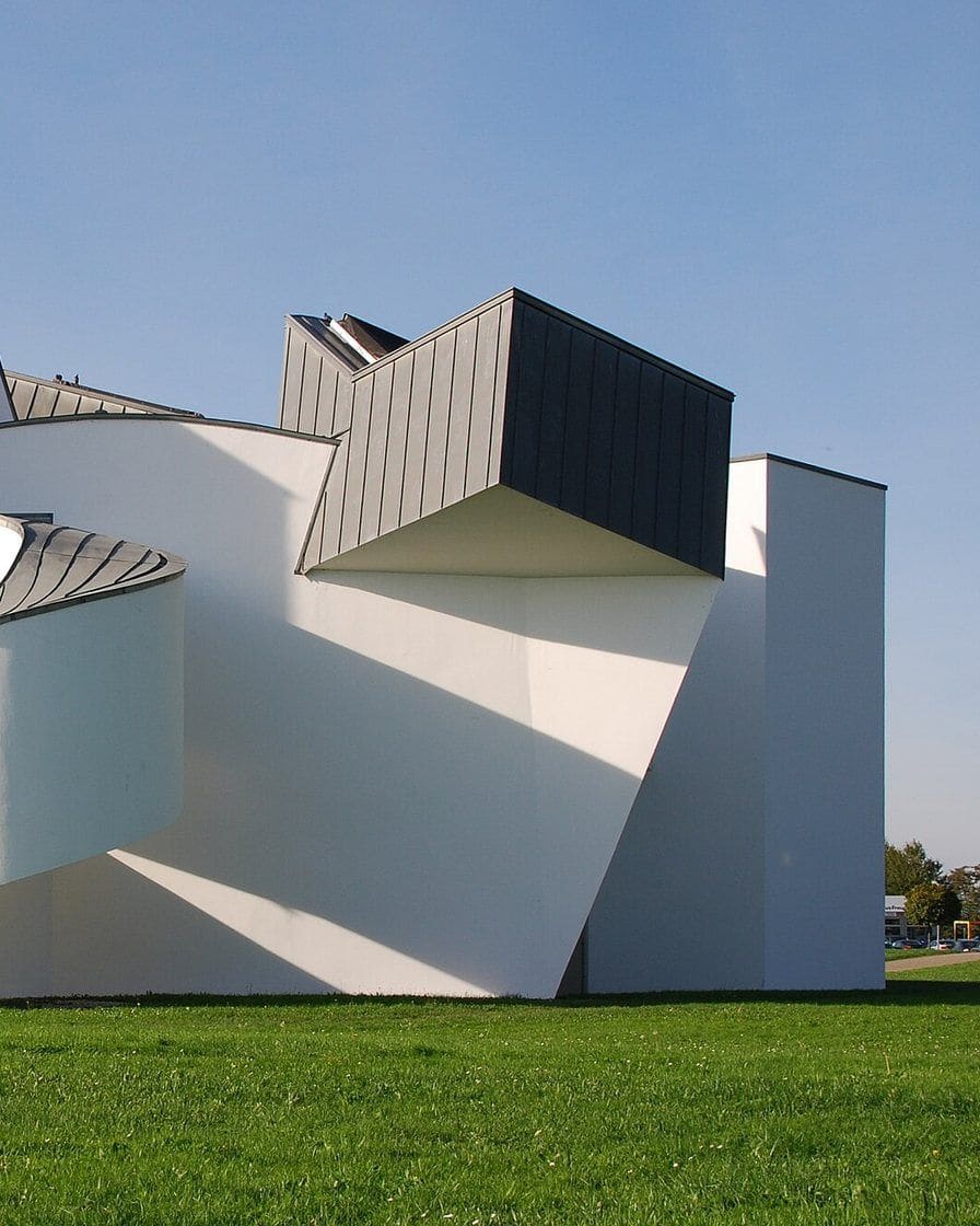Das Vitra Design Museum in Weil am Rhein bei Basel, ein weisser Bau von Frank Gehry mit geschwungenen und schräg gestellten Volumen vor blauem Himmel