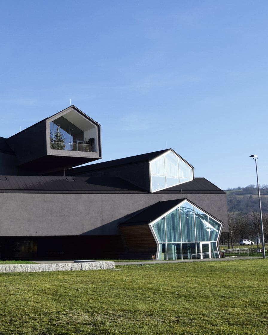 Herzog and de Meuron's VitraHaus in Weil am Rhein, stacked dark house volumes with gable roofs and large glass gable ends, with a lawn in front